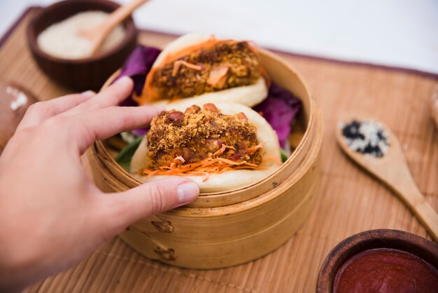 Nahaufnahme der Hand einer Person, die Taiwans traditionellen Lebensmittel Gua Bao im Dampfer hält