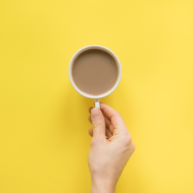 Nahaufnahme der Hand einer Person, die Tasse Kaffee über gelbem Hintergrund hält