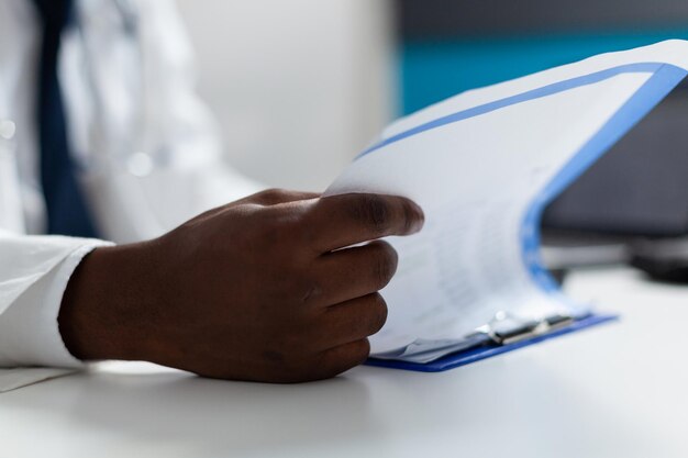 Nahaufnahme der Hand eines afroamerikanischen Arztes, der Krankheitsexpertise analysiert und medizinische Behandlung in die Zwischenablage schreibt