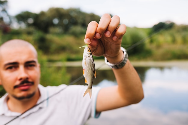 Nahaufnahme der Hand eines Fischers, die frische gefangene Fische nahe See hält