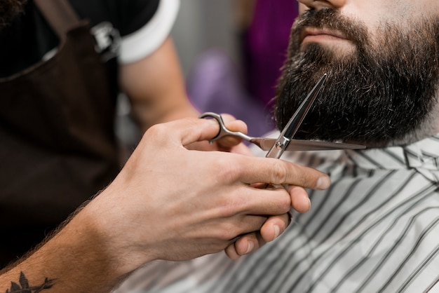 Nahaufnahme der Hand eines Friseurs, die den Bart des Mannes mit Scheren schneidet