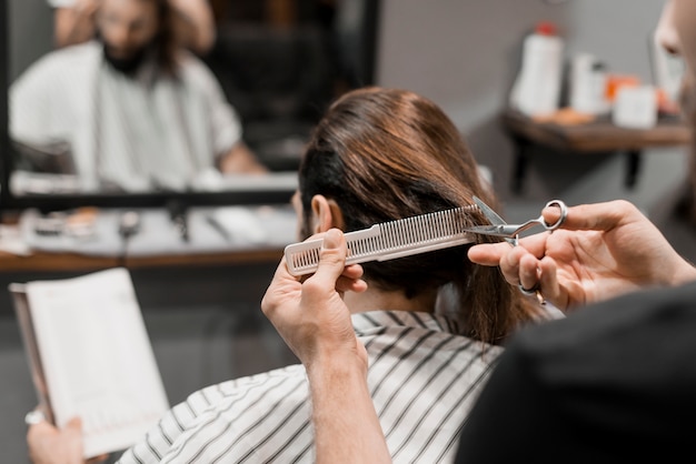 Nahaufnahme der Hand eines Friseurs, welche das Haar des männlichen Kunden mit Scheren schneidet