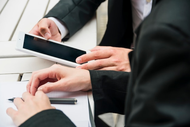 Nahaufnahme der Hand eines Geschäftsleuten mit Handy; Stift und Dokument auf dem Tisch