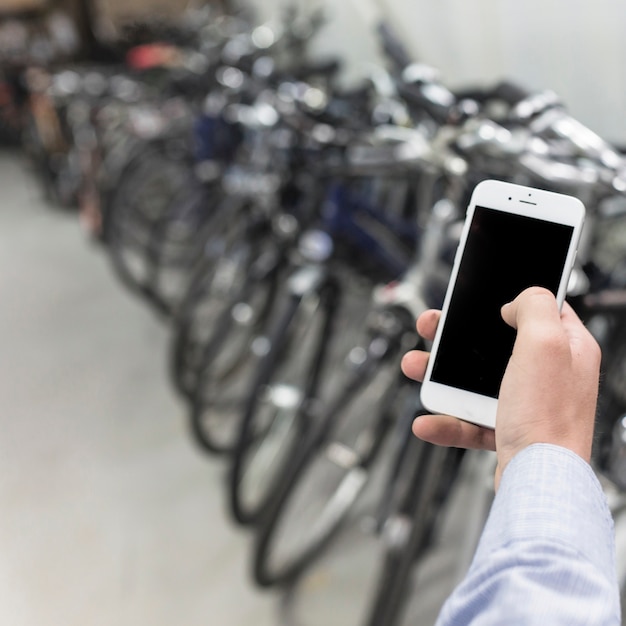 Nahaufnahme der Hand eines Mannes unter Verwendung des Mobiltelefons in der Fahrradwerkstatt