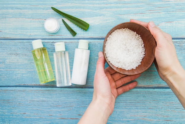 Nahaufnahme der hand schüssel steinsalze mit aloevera sprühflaschen und sahne halten