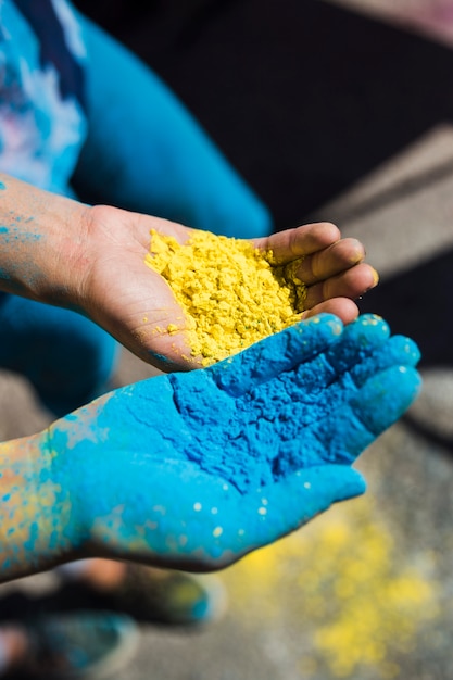 Nahaufnahme der Hand zwei Frauen, die gelbe und blaue holi Farbe anhält