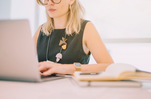 Nahaufnahme der jungen Geschäftsfrau, die Laptop mit Tagebuch am Arbeitsplatz verwendet