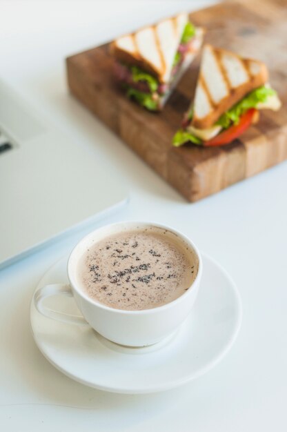 Nahaufnahme der Kaffeetasse mit Sandwichen auf hölzernem hackendem Brett