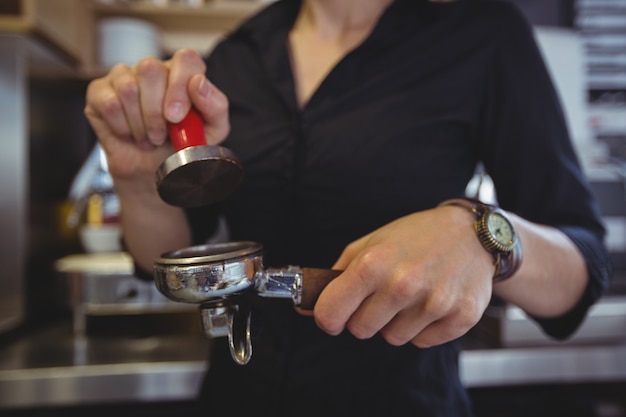 Nahaufnahme der Kellnerin, die einen Stampfer verwendet, um gemahlenen Kaffee in einen Siebträger zu drücken