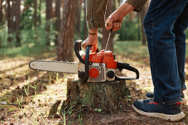 Nahaufnahme der Kettensäge auf Holzstumpf, gesichtslose Holzfäller-Startsäge