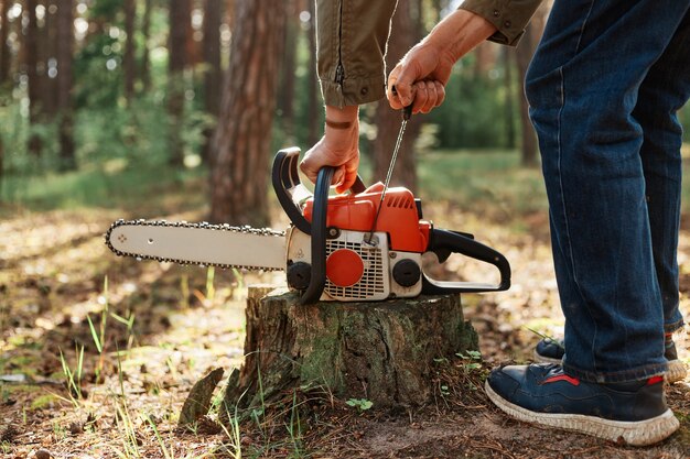 Nahaufnahme der Kettensäge auf Holzstumpf, gesichtslose Holzfäller-Startsäge