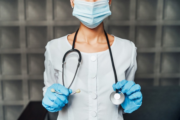 Nahaufnahme der Krankenschwester in Schutzmaske, mit Stethoskop und Schutzhandschuhen.
