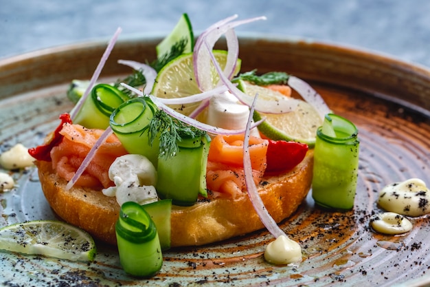 Nahaufnahme der Lachsbruschetta mit Gurken-Mozzarella-Dill-Zwiebel-getrockneten Tomaten und Limette