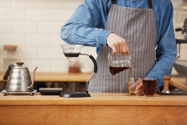 Kostenloses Foto nahaufnahme der männlichen barista-hände, die alternativen kaffee von chemex gießen.