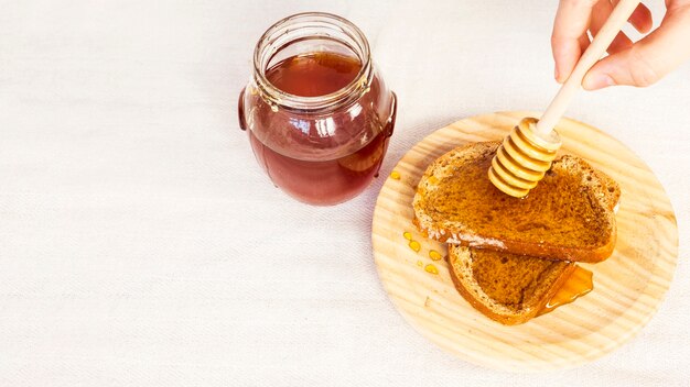 Nahaufnahme der menschlichen Hand Honig auf Brot unter Verwendung des Honigschöpflöffels ausbreitend
