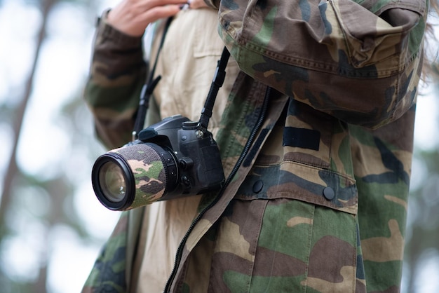 Nahaufnahme der modernen schwarzen Kamera. Digitalkamera mit großem Objektiv auf Spitze gegen Mantel im Militärstil. Technologie, Hobbykonzept