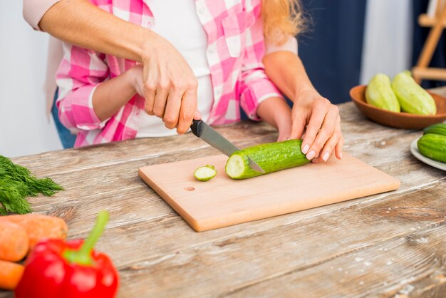 Nahaufnahme der Mutter die Hand der Tochter für das Schneiden der Gurke auf Tabelle halten