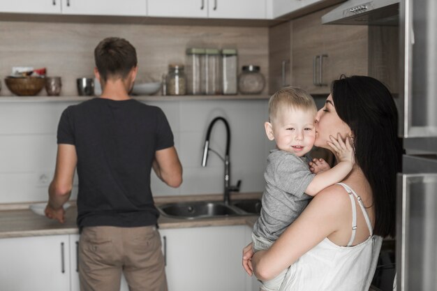 Nahaufnahme der Mutter ihren Sohn mit ihrem Ehemann liebend, der in der Küche arbeitet