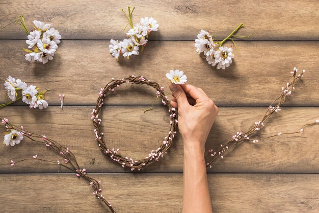 Nahaufnahme der Person Blumen- und Zweigkranz auf Holztisch machend