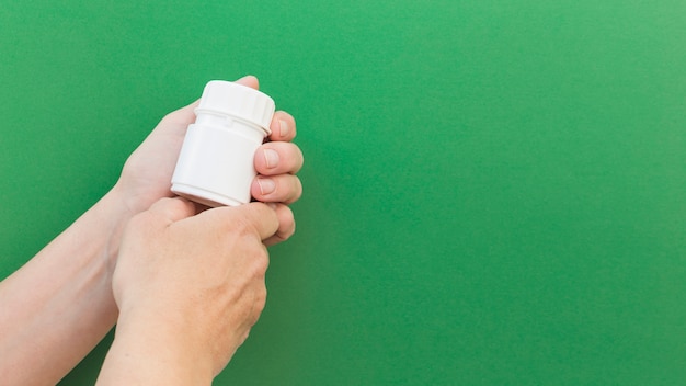 Nahaufnahme der Pillenplastikflasche der Hand gegen grünen Hintergrund