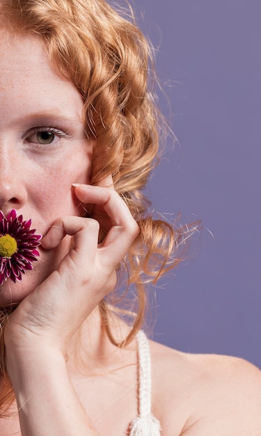 Nahaufnahme der rothaarigen Frau, die mit einer Blume auf ihrem Mund aufwirft