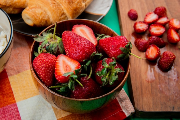 Nahaufnahme der Schüssel Erdbeeren mit Halbmondrolle in Platte auf Stoff und schneiden Erdbeeren auf Schneidebrett