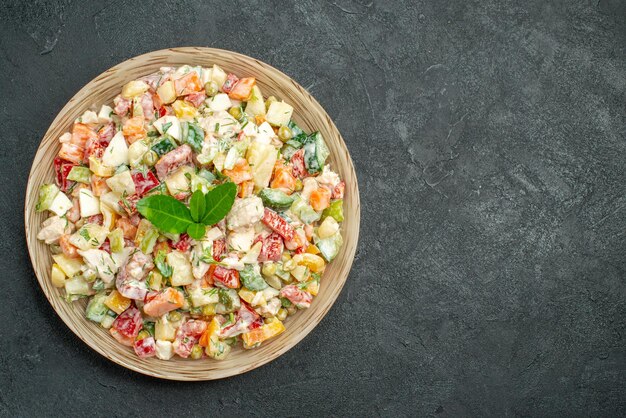 Nahaufnahme der Schüssel mit Gemüsesalat auf der linken Seite mit Grün auf dunkelgrünem Hintergrund