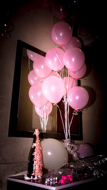 Nahaufnahme der Sektflasche mit rosa Ballonen auf Schreibtisch