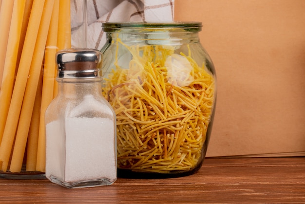 Nahaufnahme der Spaghetti-Nudeln in Glas und Salz mit Bucatini-Nudeltuch und Notizblock auf Holzoberfläche