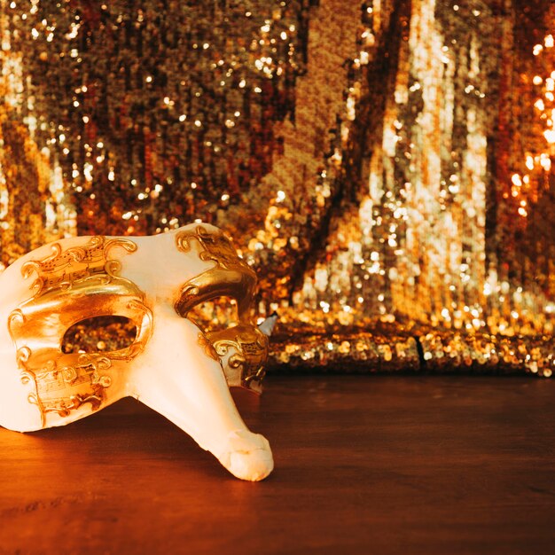 Nahaufnahme der venetianischen weißen Karnevalsmaske auf Holztisch gegen Paillettengewebe