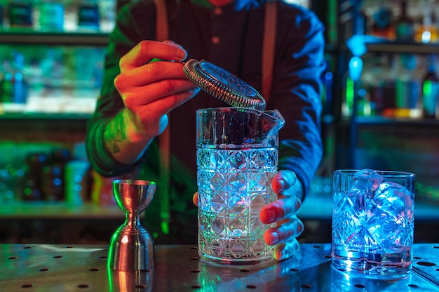 Nahaufnahme des Barmanns beendet die Zubereitung von alkoholischen Cocktails in buntem Neonlicht