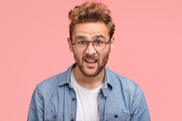 Nahaufnahme des betäubten empörten Mannes mit lockigem Haar, schaut verzweifelt in die Kamera, trägt runde Brille für gute Sicht