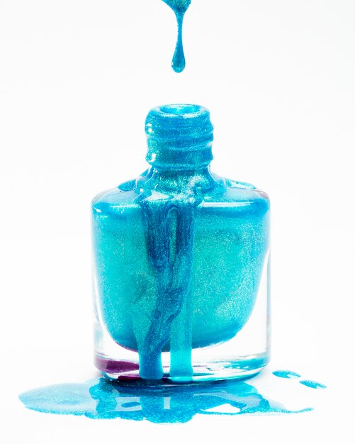 Nahaufnahme des blauen Funkelnnagellacks, der in seine Flasche gegen einen weißen Hintergrund fällt