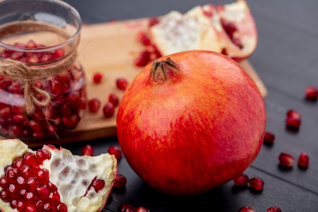 Kostenloses Foto nahaufnahme des ganzen granatapfels und des granatapfelstückes mit beeren auf schwarzer wand