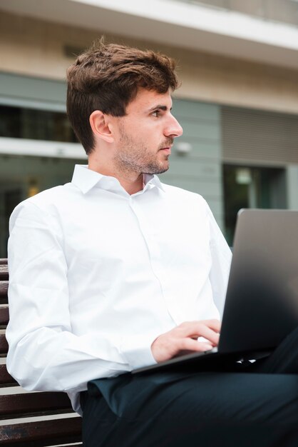 Nahaufnahme des Geschäftsmannes unter Verwendung auf dem Laptop, der weg schaut