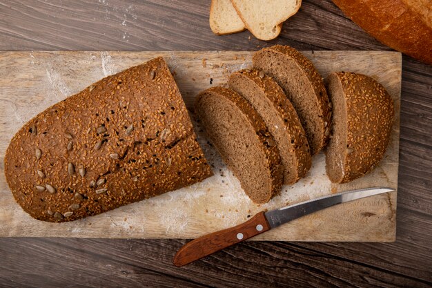 Nahaufnahme des geschnittenen und geschnittenen Sandwichbrotes mit Messer auf Schneidebrett auf hölzernem Hintergrund