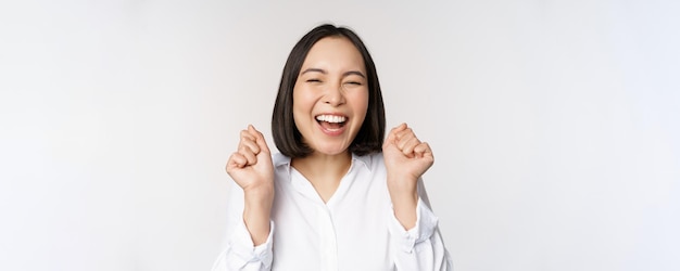 Nahaufnahme des Gesichtsporträts einer tanzenden asiatischen Frau, die triumphierend lächelt und mit fröhlichen Emotionen feiert, die über weißem Hintergrund stehen. Kopieren Sie Platz