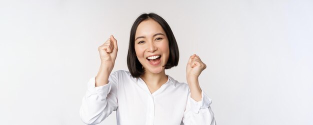 Nahaufnahme des Gesichtsporträts einer tanzenden asiatischen Frau, die triumphierend lächelt und mit fröhlichen Emotionen feiert