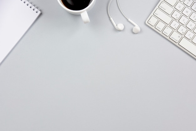 Nahaufnahme des gewundenen Notizblockes; Kaffeetasse; Kopfhörer und Tastatur auf grauem Hintergrund