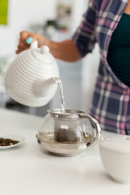 Nahaufnahme des Gießens von heißem Wasser über natürliche aromatische Kräuter, um Tee zuzubereiten