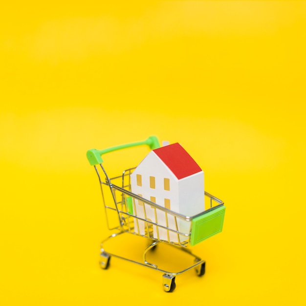 Nahaufnahme des Hausmodells im Miniaturwarenkorb gegen gelben Hintergrund