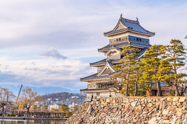 Nahaufnahme des historischen Schlosses Matsumoto mit einer Steinmauer und schönen Bäumen an einem wolkigen Tag