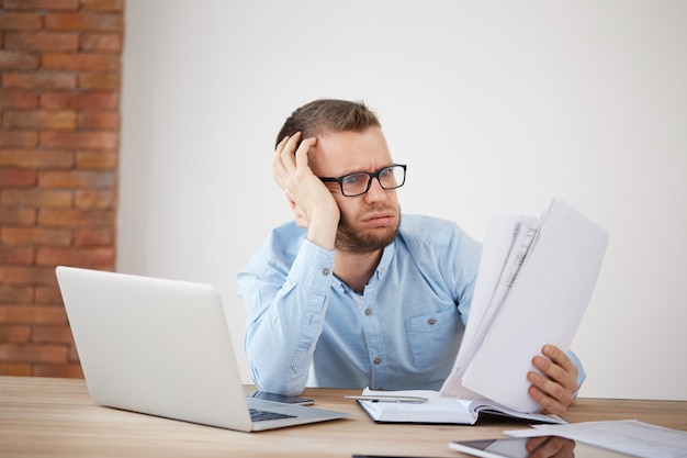 Kostenloses Foto nahaufnahme des jungen erschöpften unglücklichen bärtigen männlichen finanzmanagers, der spät abends im büro sitzt