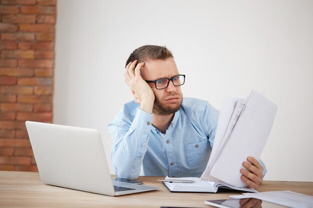 Nahaufnahme des jungen erschöpften unglücklichen bärtigen männlichen Finanzmanagers, der spät abends im Büro sitzt