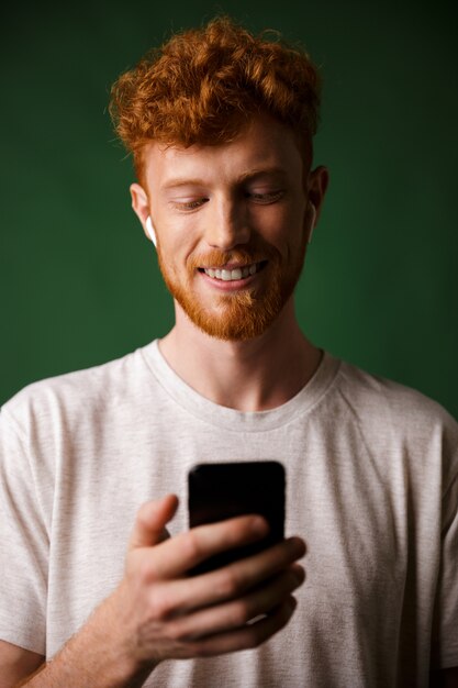 Nahaufnahme des jungen fröhlichen rothaarigen bärtigen jungen Mannes, Musik mit Airpods hörend