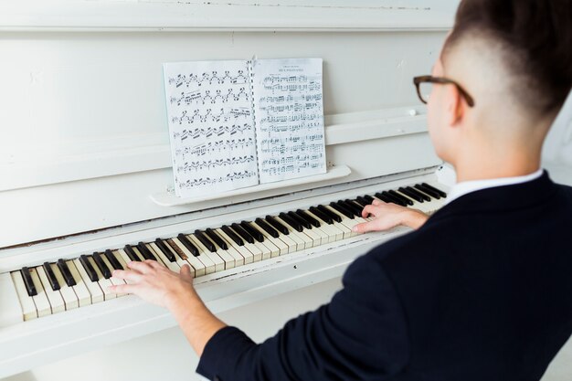 Nahaufnahme des jungen Mannes das musikalische Blatt betrachtend, das Klavier spielend