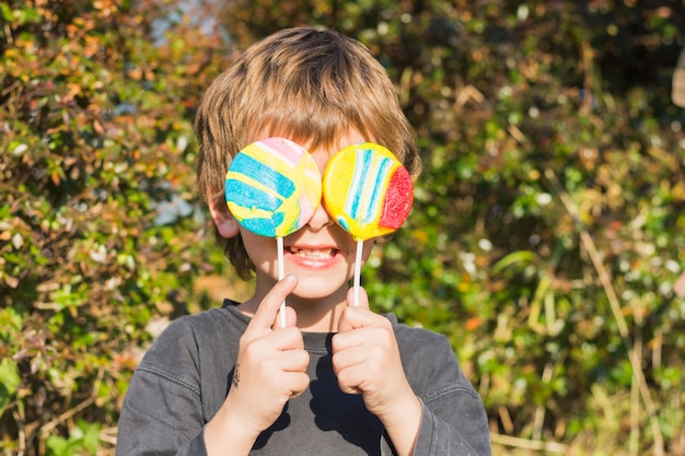 Nahaufnahme des Jungen zwei Lutscher vor seinen Augen halten