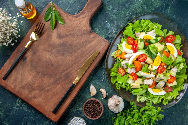 Nahaufnahme des köstlichen Salats mit vielen frischen Zutatengewürzen Ölflasche Knoblauchbesteck auf Holzschneidebrett gesetzt