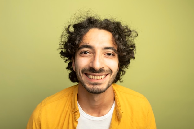 Nahaufnahme des lächelnden jungen hübschen kaukasischen Mannes, der Kamera lokalisiert auf olivgrünem Hintergrund betrachtet