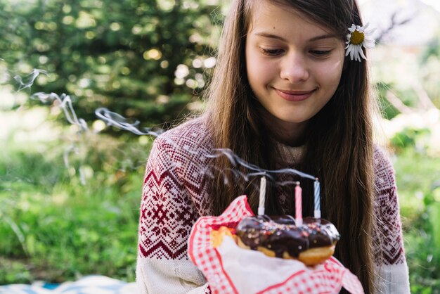 Nahaufnahme des lächelnden Mädchens, das betrachtet, löschen Kerzen über dem Donut